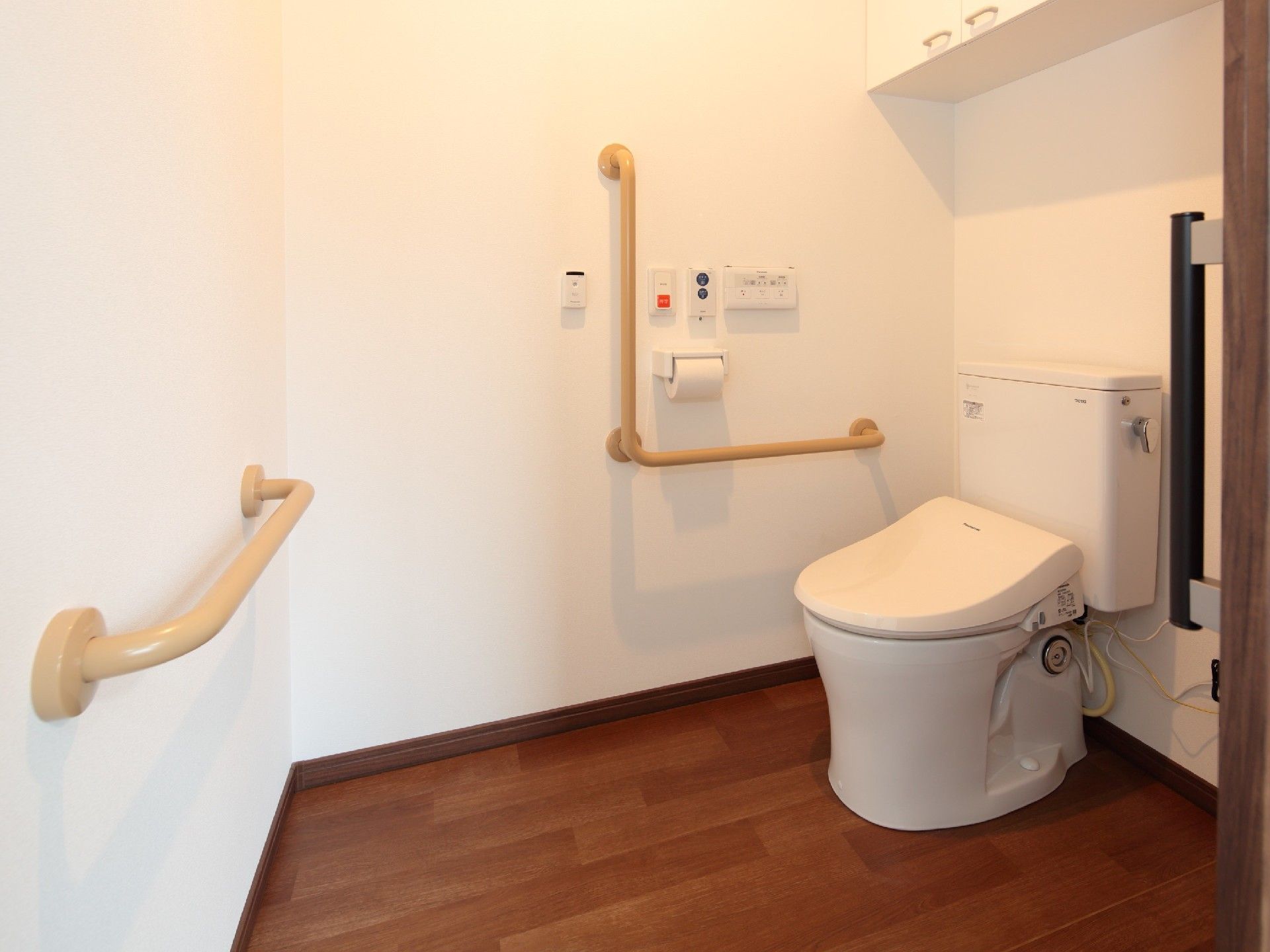 白を基調としたトイレには手すりや呼び出しボタンも付き、棚もある。