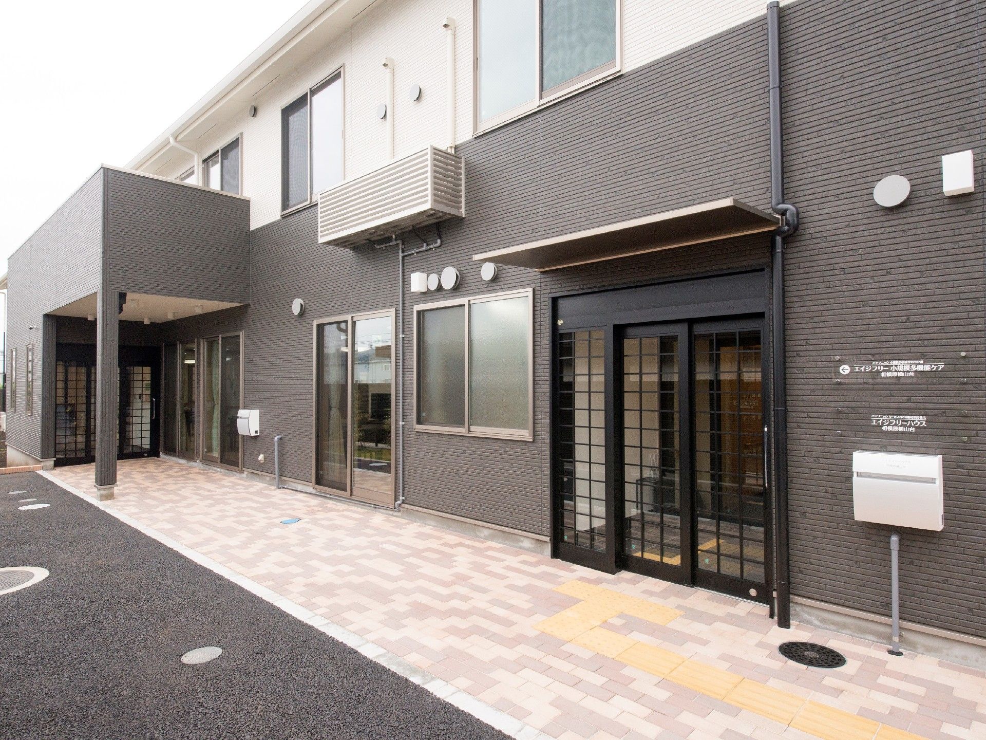 建物は2階建てで、二つ玄関が付き、建物の前にはレンガ調のブロックが敷かれ、点字ブロックも敷かれている。