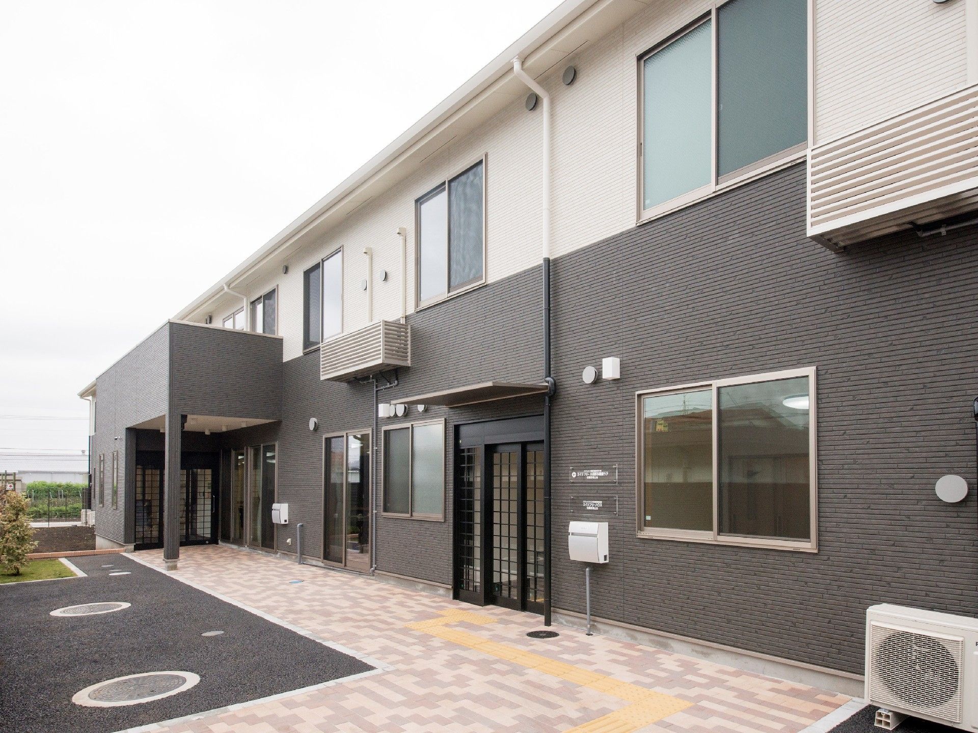 2階建ての建物の玄関には屋根が付き、グレーと白の2色づかいで落ち着いた雰囲気。