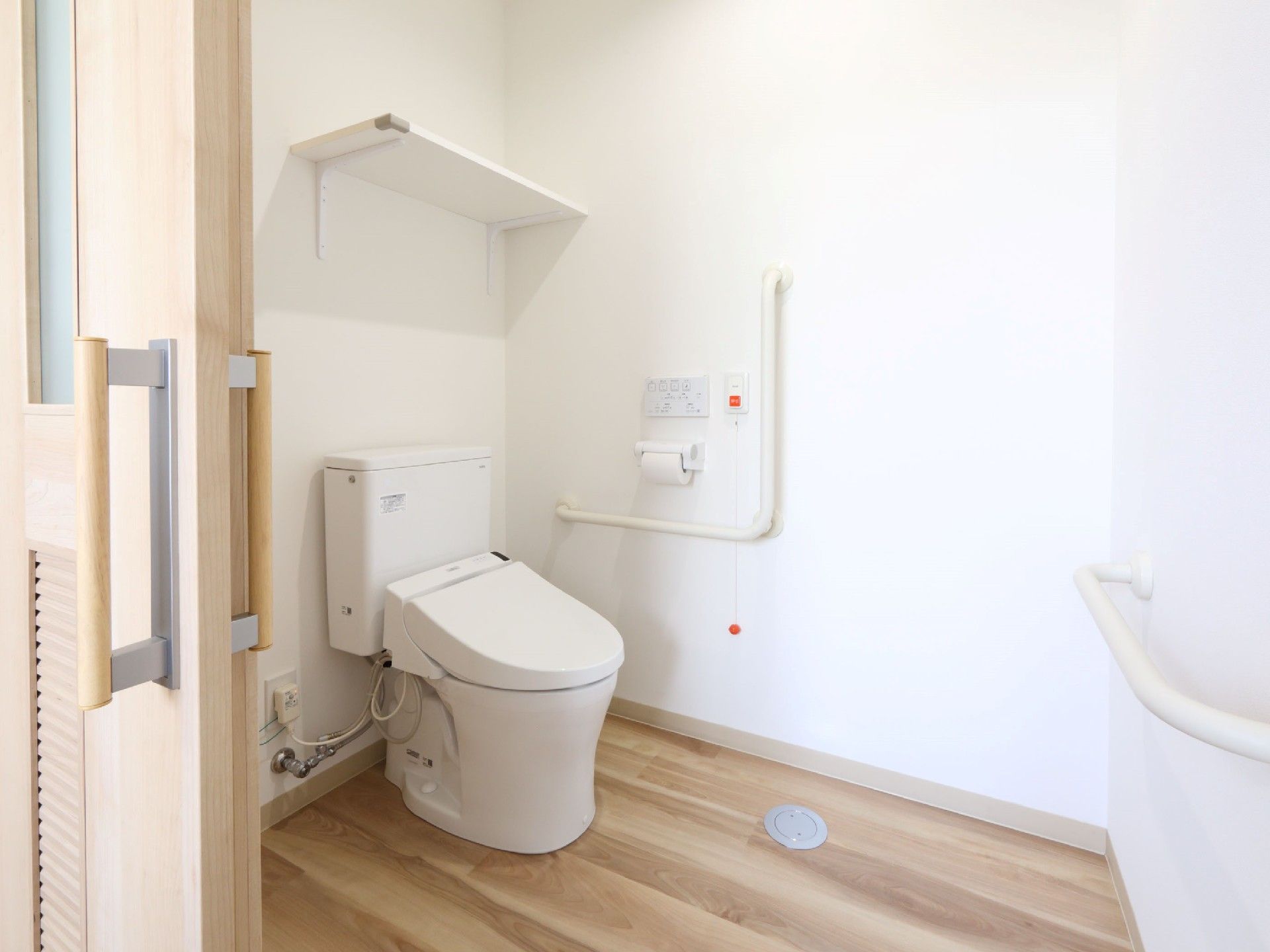 広いトイレには収納棚が付き、壁には複数の手すりと呼び出しボタンが付いている。