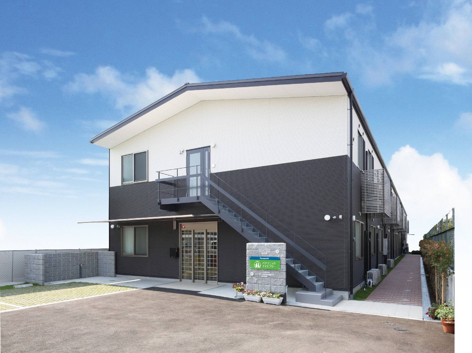 屋外階段やベランダが付いた建物は2階建てでシンプルなデザイン。広い駐車スペースもある。