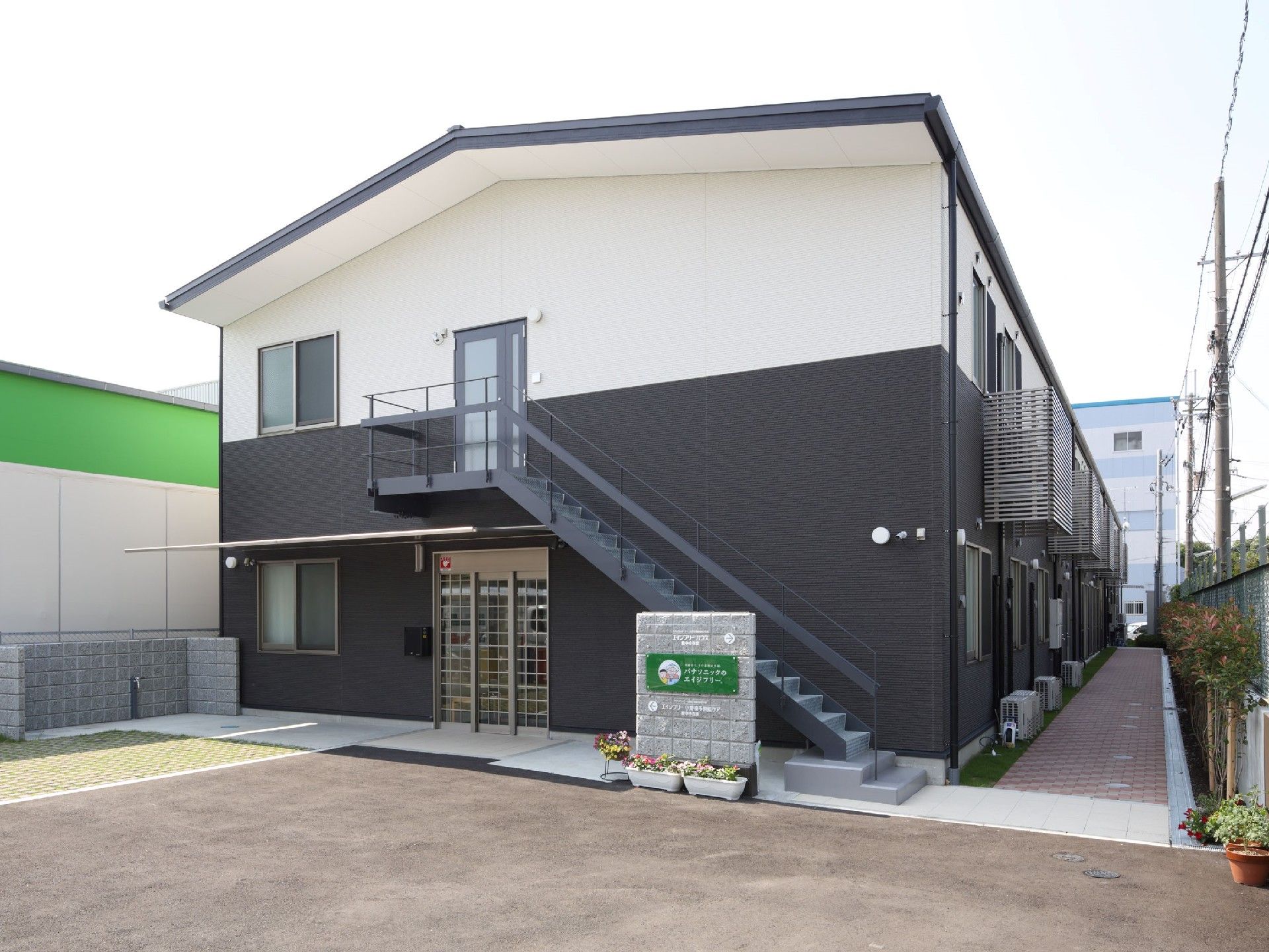 2階建ての建物。1階部分は黒、2階部分は白で、玄関の周りにはプランターも置かれている。