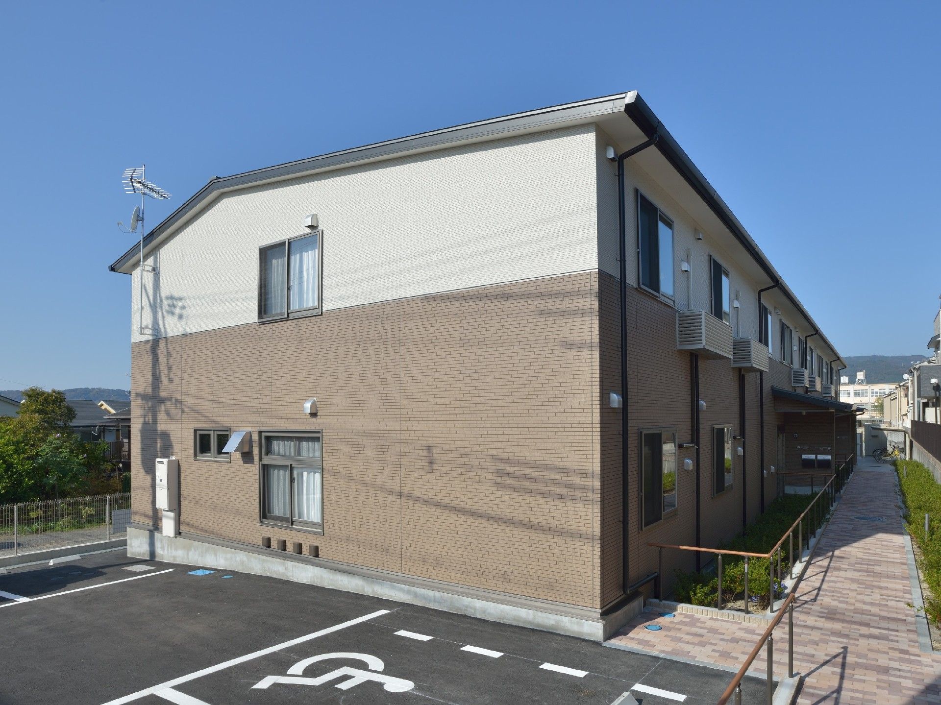 横に長い長方形の建物は2階建てで、1階がブラウン。駐車スペースもある。