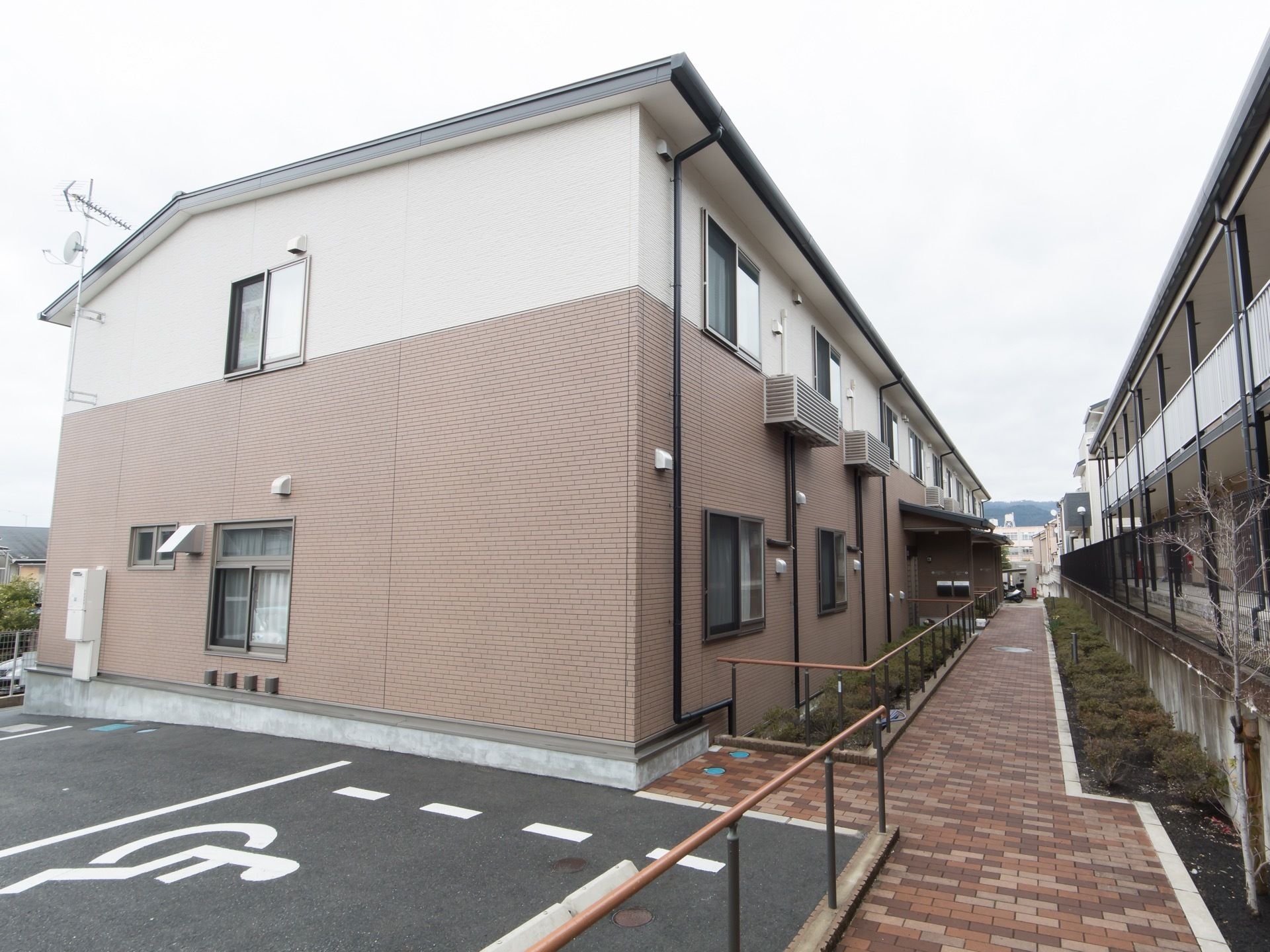 ２階建てのアットホームな雰囲気の建物である。横に駐車スペースがあり、玄関までの通路には手すりが完備されている。