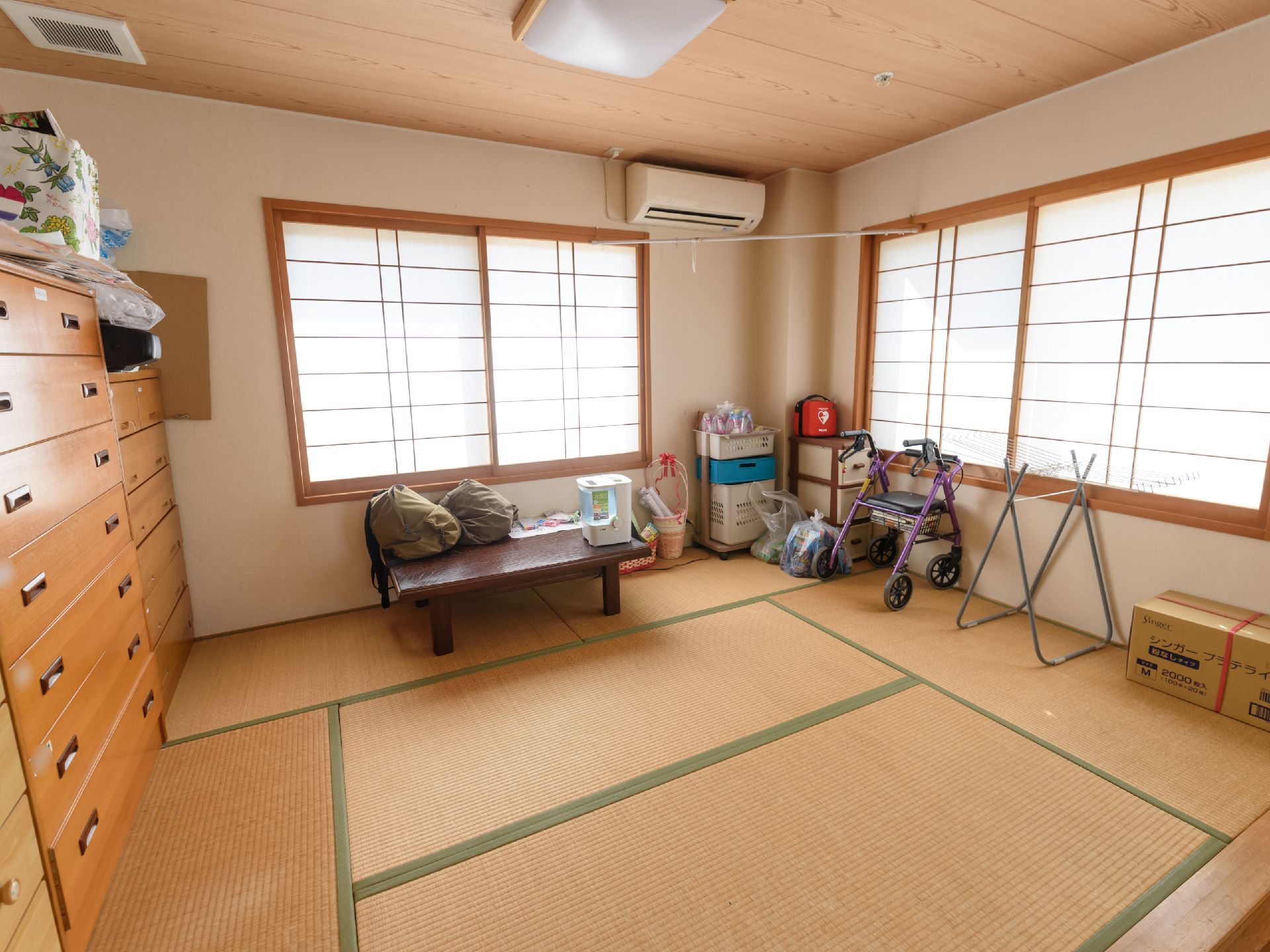 畳が敷かれており、窓の前には障子が貼られた戸がある。壁側には大きなタンスが並んで設置されており、その上に紙袋などが収納されている。