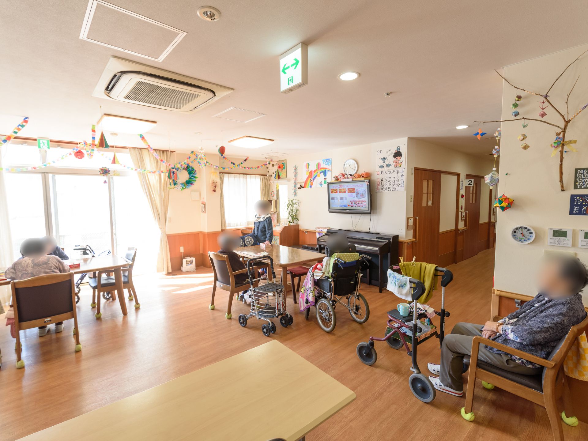 広いスペースに椅子やテーブルが設置されており、入居者様が席についている。壁にはテレビが掛けられていて、絵などが飾られている。