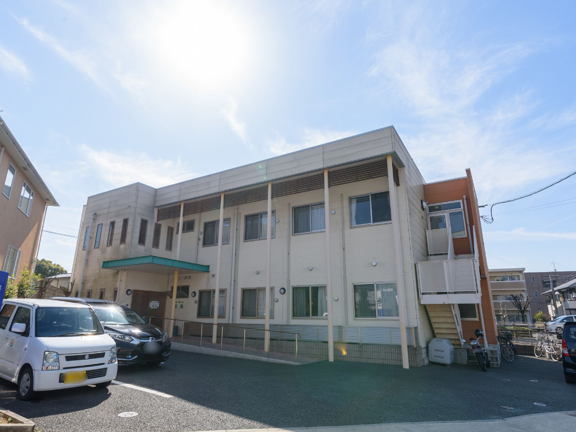 ２階建ての白い建物になっており、右側には外階段がついている。玄関の前はスロープになっていて、手すりが設置されている。