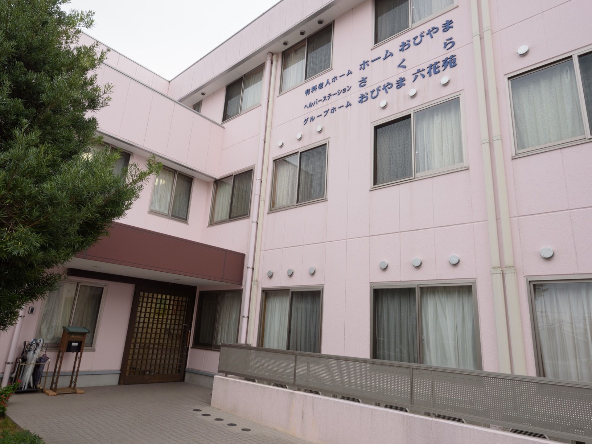 建物は３階建てで、壁には系列の施設を含む３施設の名前が記載されている。建物の前には、低めのフェンスが設置されている。