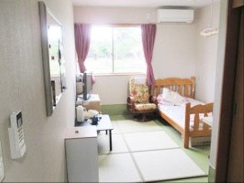 大きな窓から射し込む自然光で、明るい空間を確保した居室である。床には畳を敷設し、壁際にベッドを備えている。