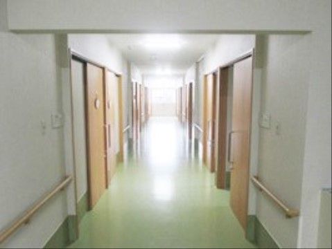 黄緑の床を取り入れた廊下スペースである。両側に木目調のドアが並び、壁に手すりを設置している。掃除が行き届いたスッキリとした印象の空間である。
