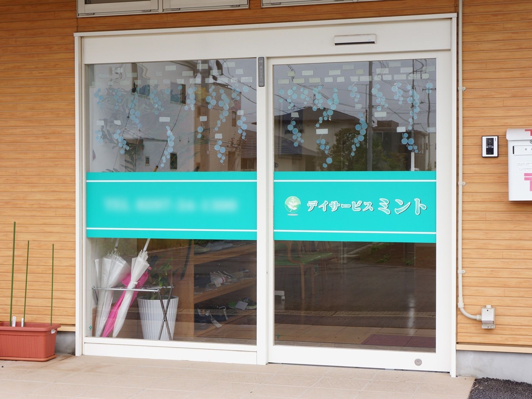 入り口はバリフリーになっており、広く開閉する自動ドアの横には木目調の壁に白の郵便ポストが取り付けられている。