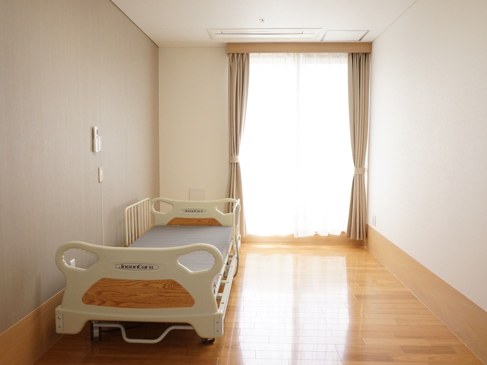ベランダから明るい光が差し込む陽当たり良い居室には、移動式のベッドが置かれており、ゆったりとしたスペースがある。