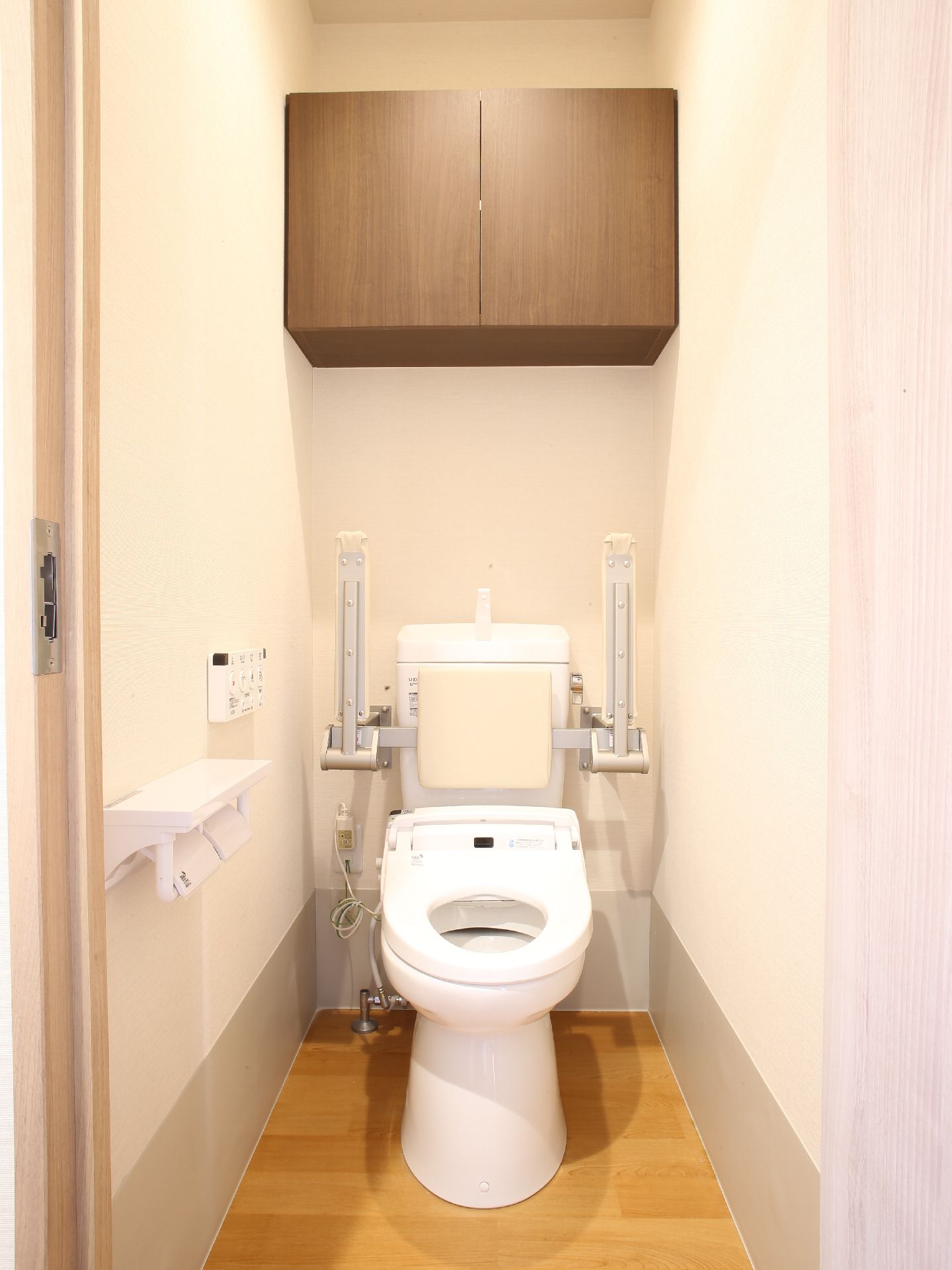 トイレにはひじ掛けがついていて、使用しないときには上にあげることができる。高い位置に収納の戸棚があるので便利。