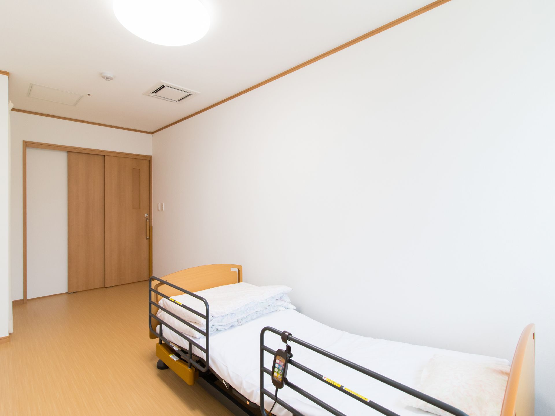 居室の様子である。ワンルームに転落防止柵が付いた介護用ベッドが置かれている。部屋の扉は引き戸になっている。