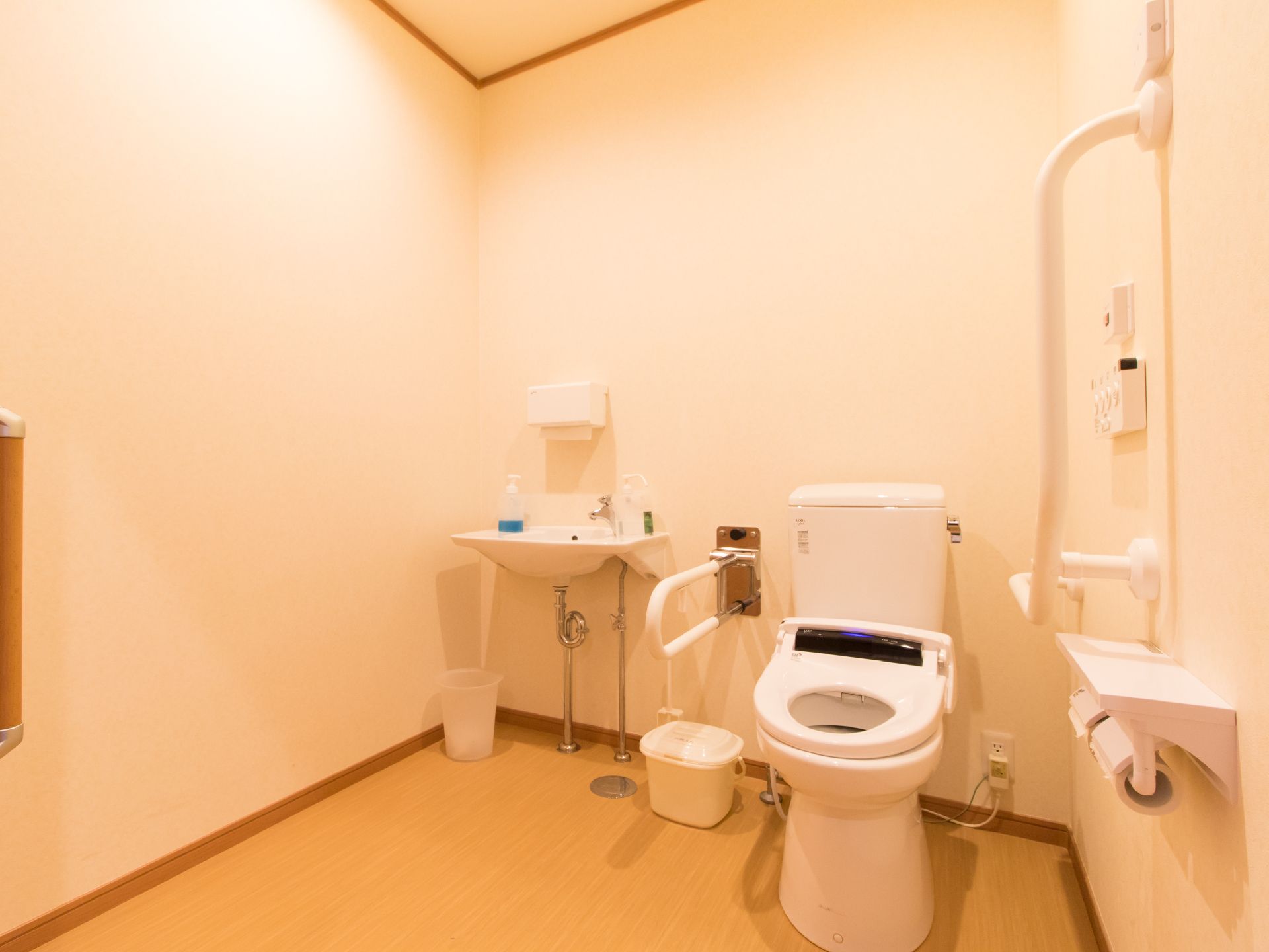 トイレの様子である。手すりが付いており、温水洗浄便座も設置されている。個室には、手洗い場も用意されている。