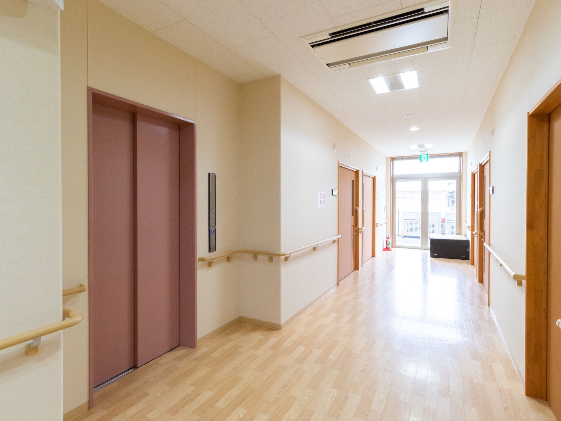 居室前の明るい廊下で、エレベーターが１基設置されている。突き当りには非常扉が設けられており、ガラス窓からは外光が差し込む。