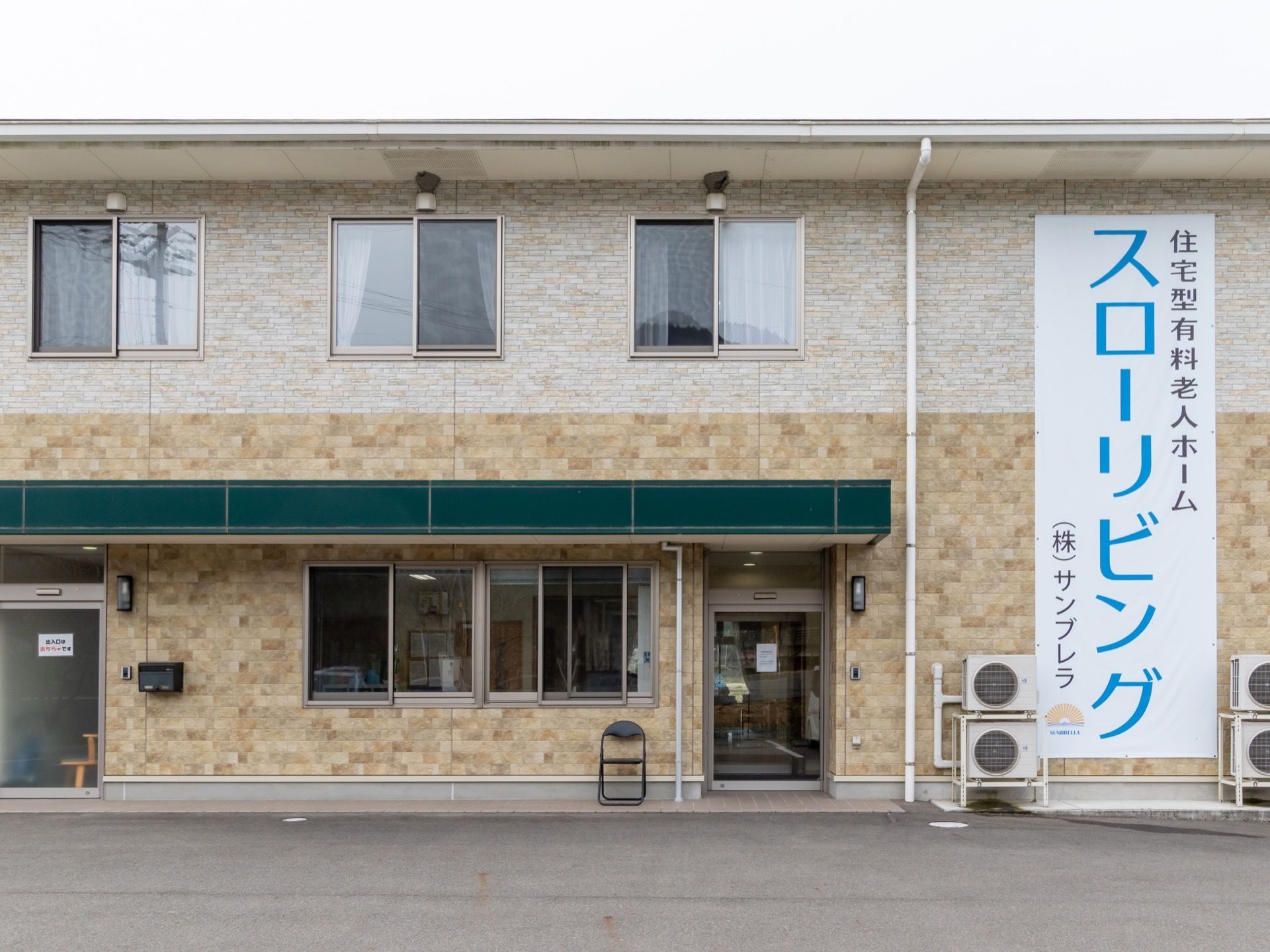 ２階建てのグループホームで、外壁に大きな文字で施設名が書かれている。エントランスが２つ設けられている。