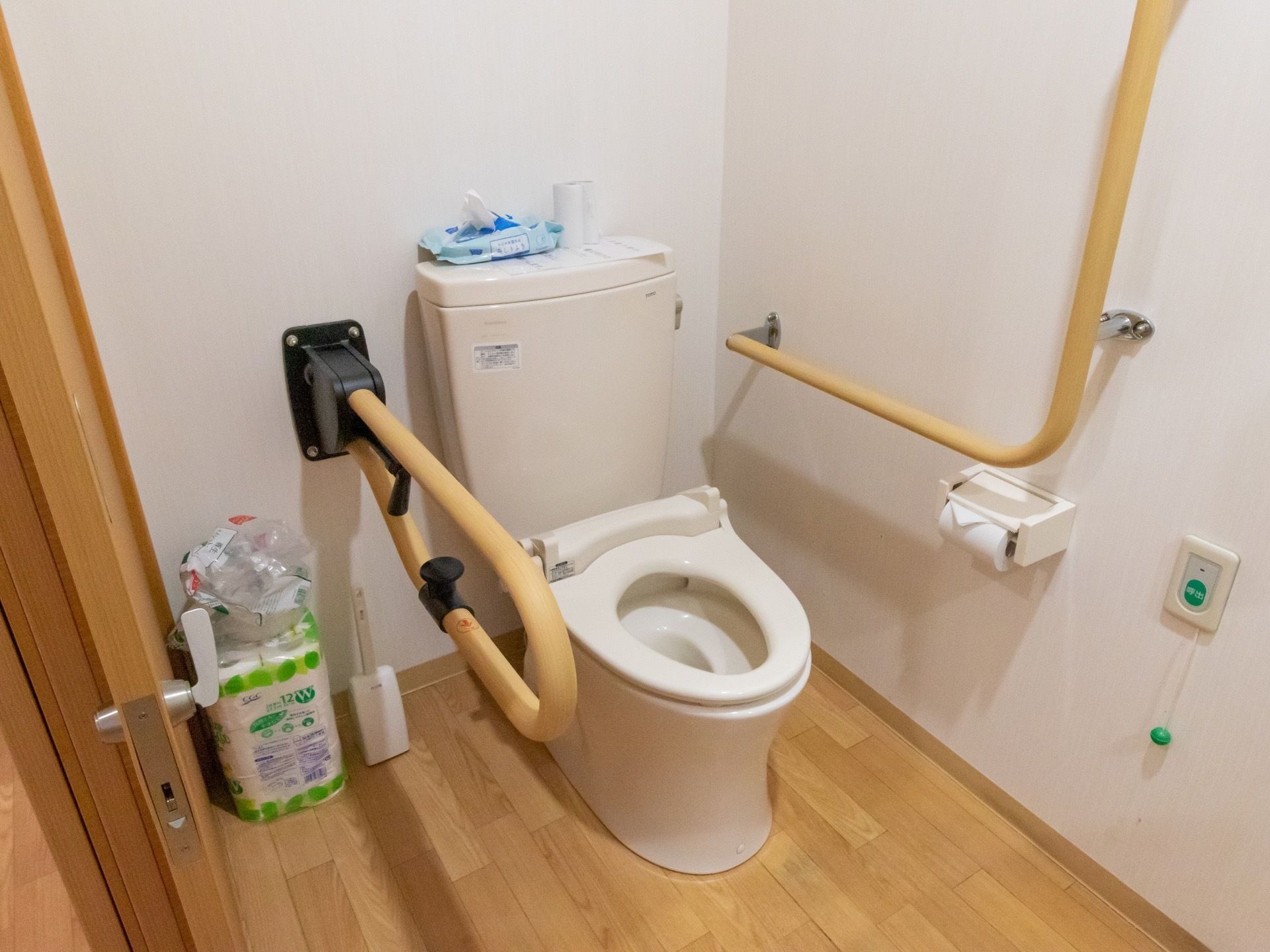 スライド式の扉で仕切られているトイレである。隅には予備のトイレットペーパーや掃除用具が置かれている。