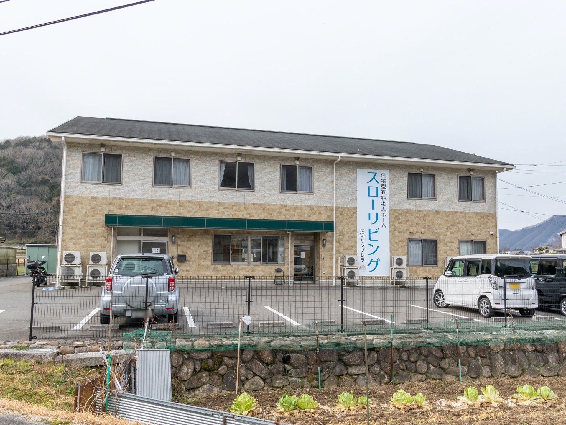 ２色で構成された外壁の２階建ての建物。建物の正面には駐車場が確保されている。