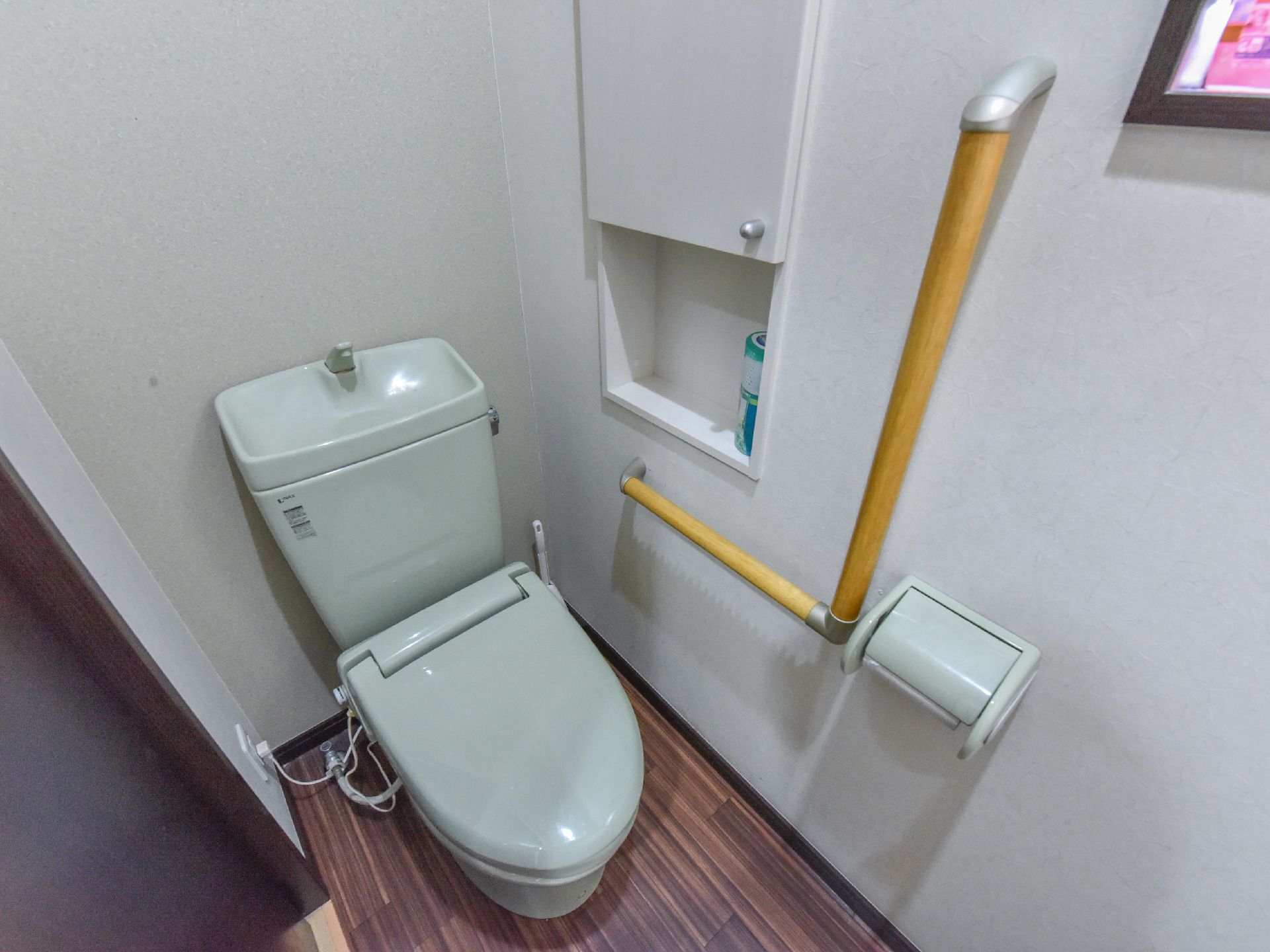 トイレ内部の様子。洋式の水洗トイレが設置され、ペーパーホルダーの隣には手すりがある。収納ボックスがトイレの左上に付けられている。
