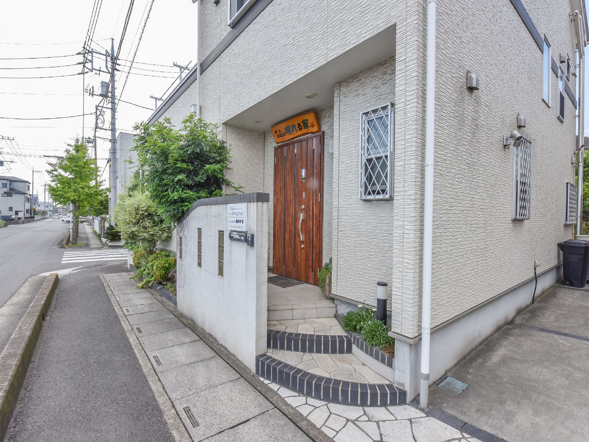 施設外観の様子。入り口まで数段の段差がある。木造り風の入り口の上には施設名の書かれたプレートが飾られている。