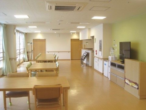 段差のない広々とした食堂に、椅子と机が並べられている。白い壁には手すりが設置され、大きな窓がある。テレビが置かれている。