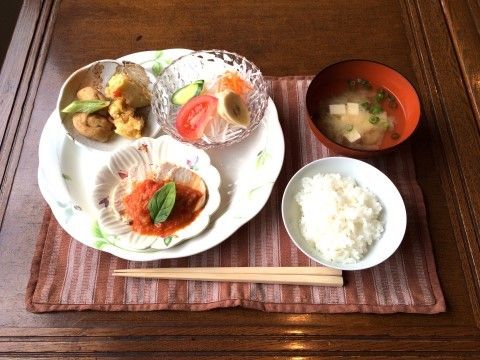 ランチョンマットが敷かれ、木製のお箸と食事が並んでいる。ご飯とみそ汁のほかに、大きな皿の上に小さな皿に入ったおかずが３種類乗っている。