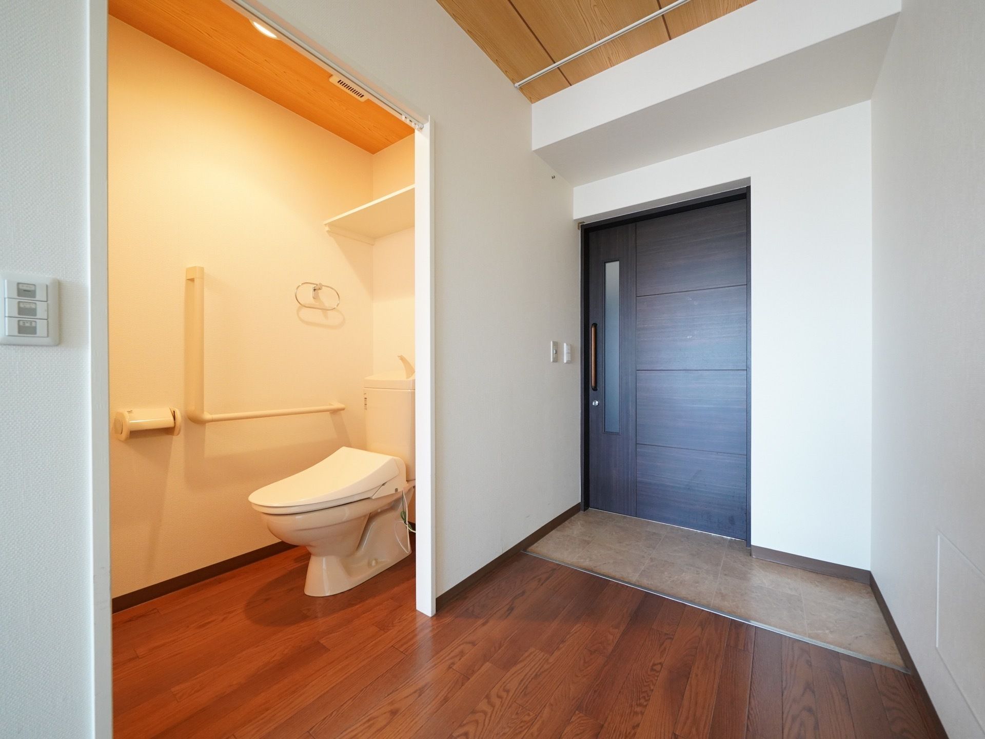 黒い居室ドアがあり、靴を脱ぐスペースがある。バリアフリーを採用している。入口横にトイレがある。壁にスイッチが設置されている。