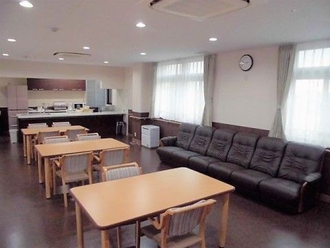 部屋の中心に３組のダイニングテーブルと椅子が置いてある。レースカーテンが掛けられた窓際に、６人掛けのソファーが設置されている。