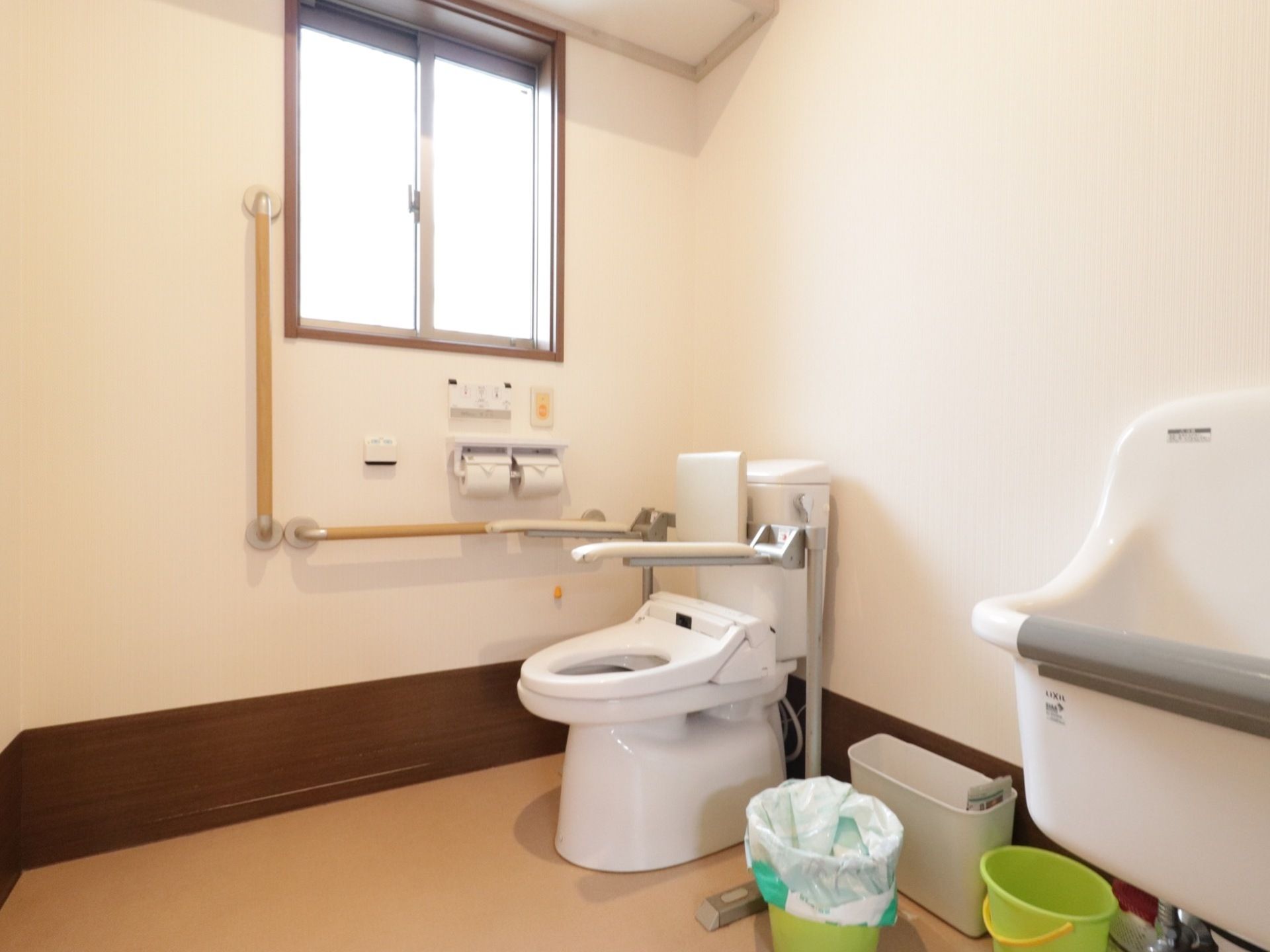 窓がある明るいトイレになっている。温水洗浄便座になっており、操作ボタンが壁にあるので押しやすく便利である。壁にL字型の手すりを設置している。