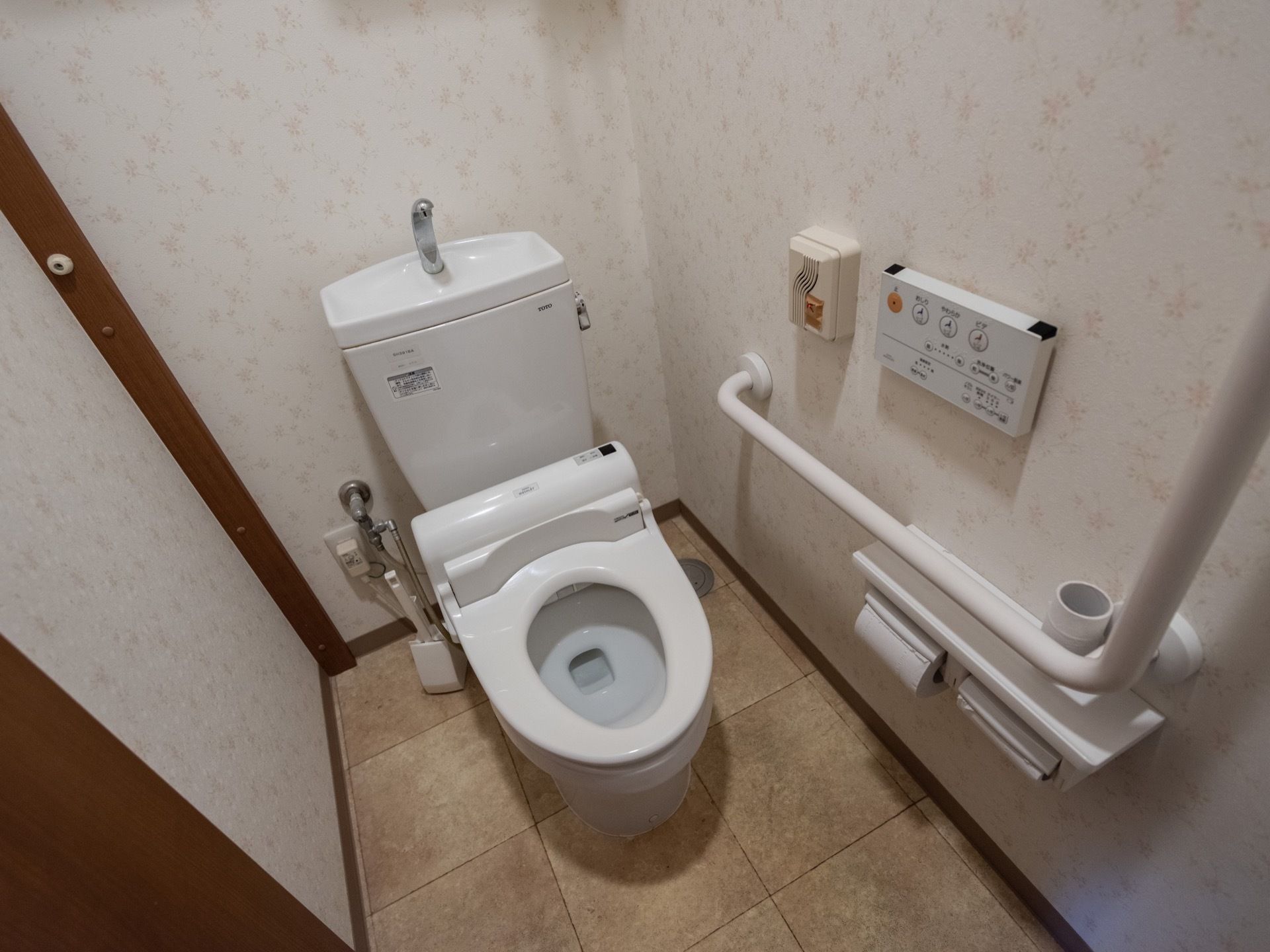 洋式の白い便器が１つあり、便器のタンクの上は手洗い場になっている。壁には手すりとインターホン、温水洗浄便座のリモコンなどが設置されている。
