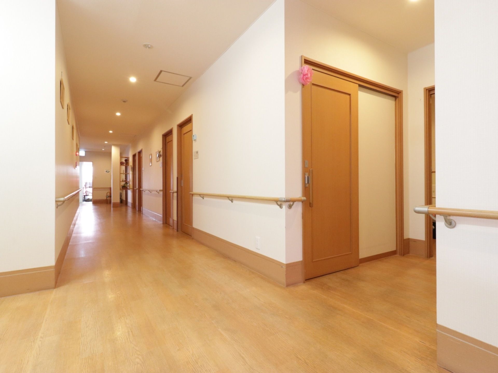 廊下の壁と天井は白色で、廊下は木目調である。廊下の両側には居室のドアが並び、手すりが設置されている。