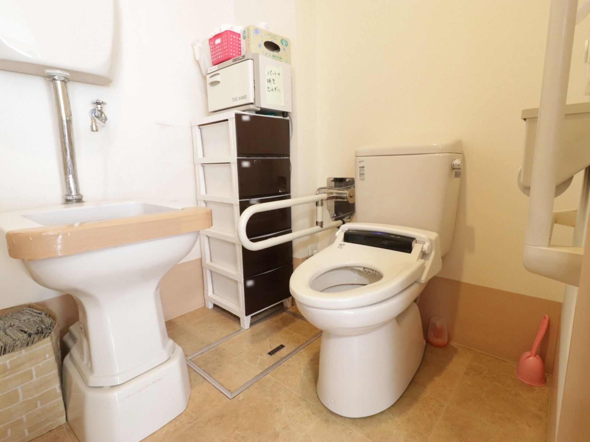 広々としたトイレには、洋式便器とオストメイト用便器が設置されている。可動式の手すりが壁に取り付けられている。