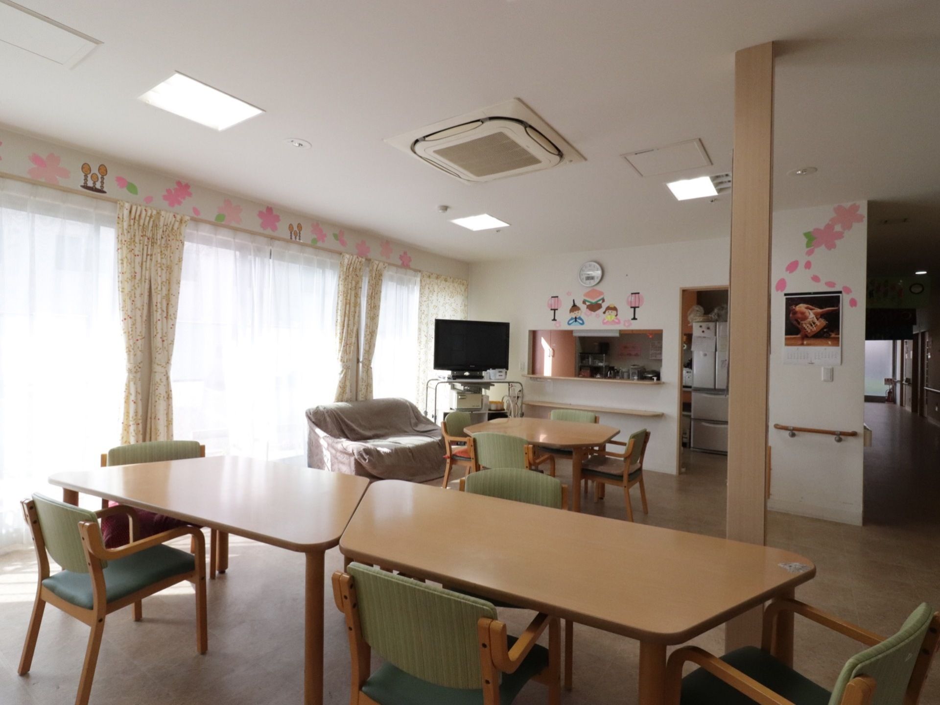 広々とした食堂には、入居者様人数分の椅子がセットされたダイニングテーブルが用意されている。ソファやテレビが置かれている。
