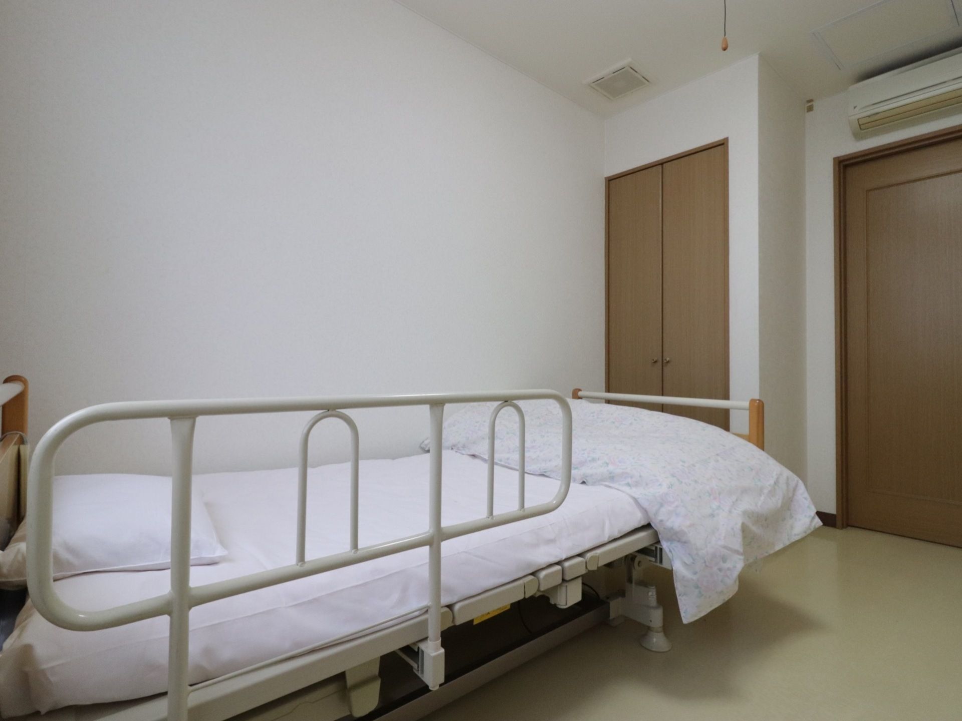 部屋の縦の広さは、ベッドを１台設置するのにちょうど良い。転倒を防止する柵が付いた、電動で動く背もたれのベッドを置いてある。