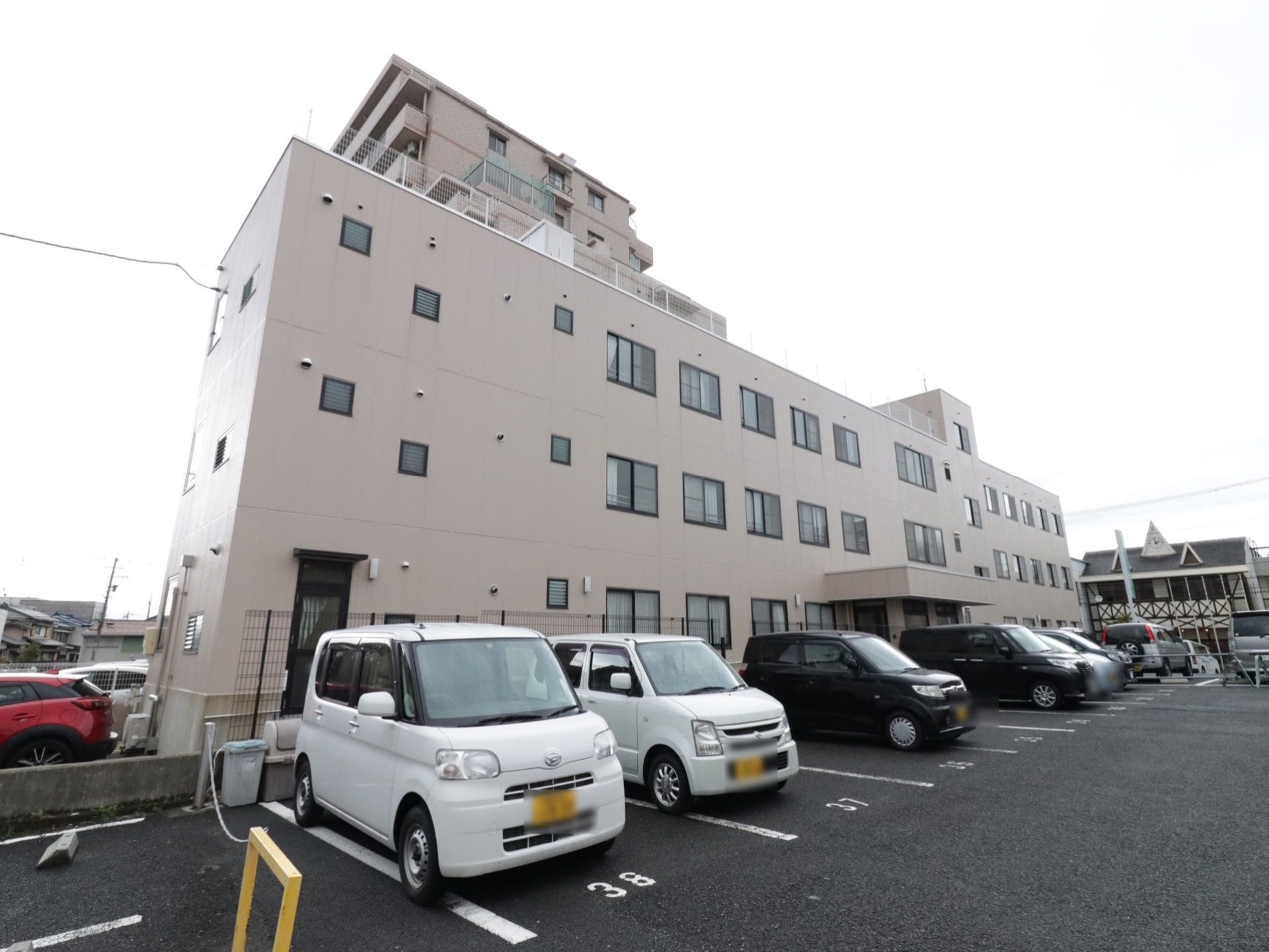 薄い茶色の外壁を持つ、３階建ての施設である。入口前には、黒いフェンスがあり駐車場との間を隔てている。