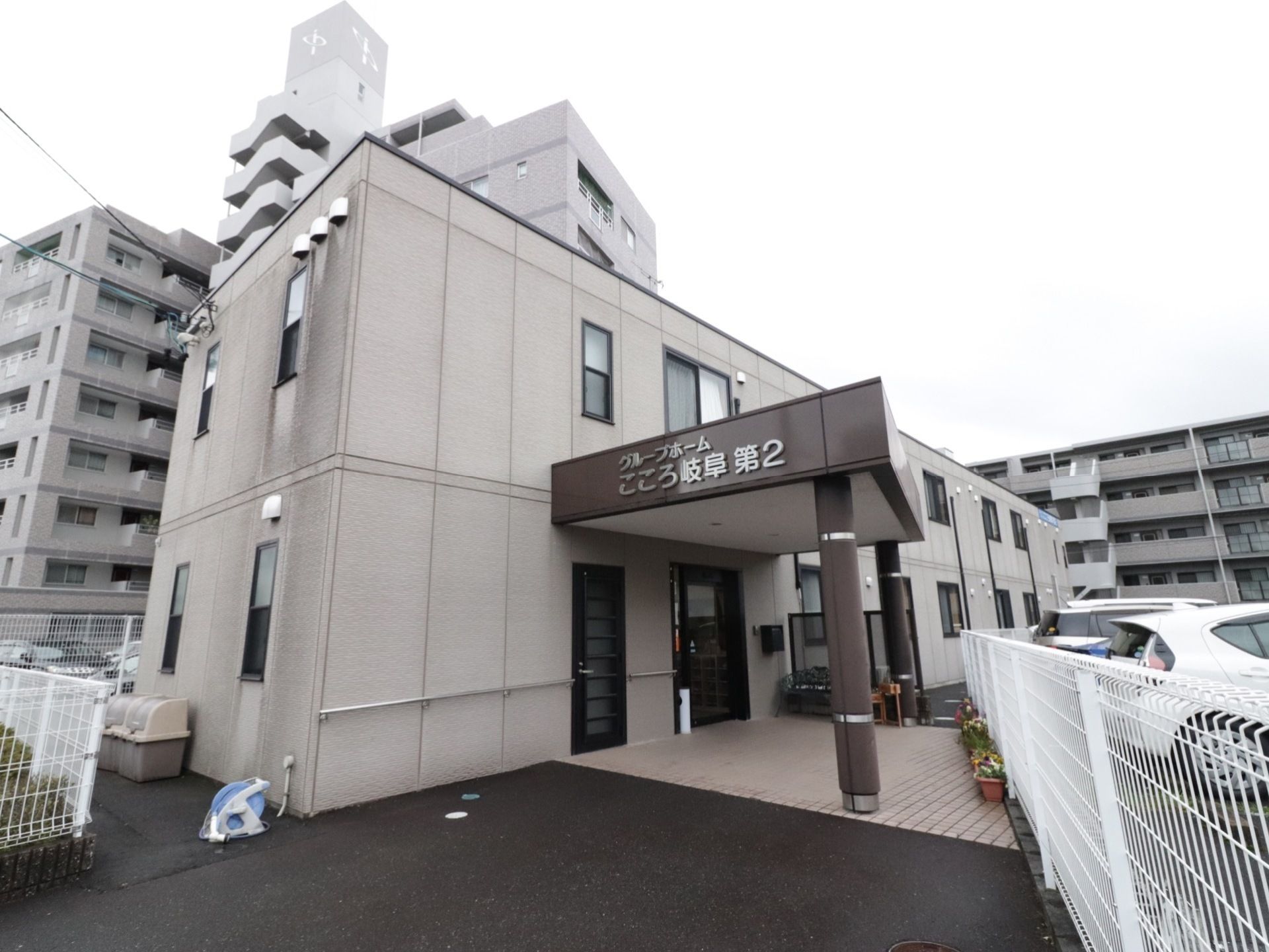建物の周りには、白い格子の柵を張り巡らせている。玄関前の屋根には、横側から歩いて来た時にも見えるように施設名が設置されている。