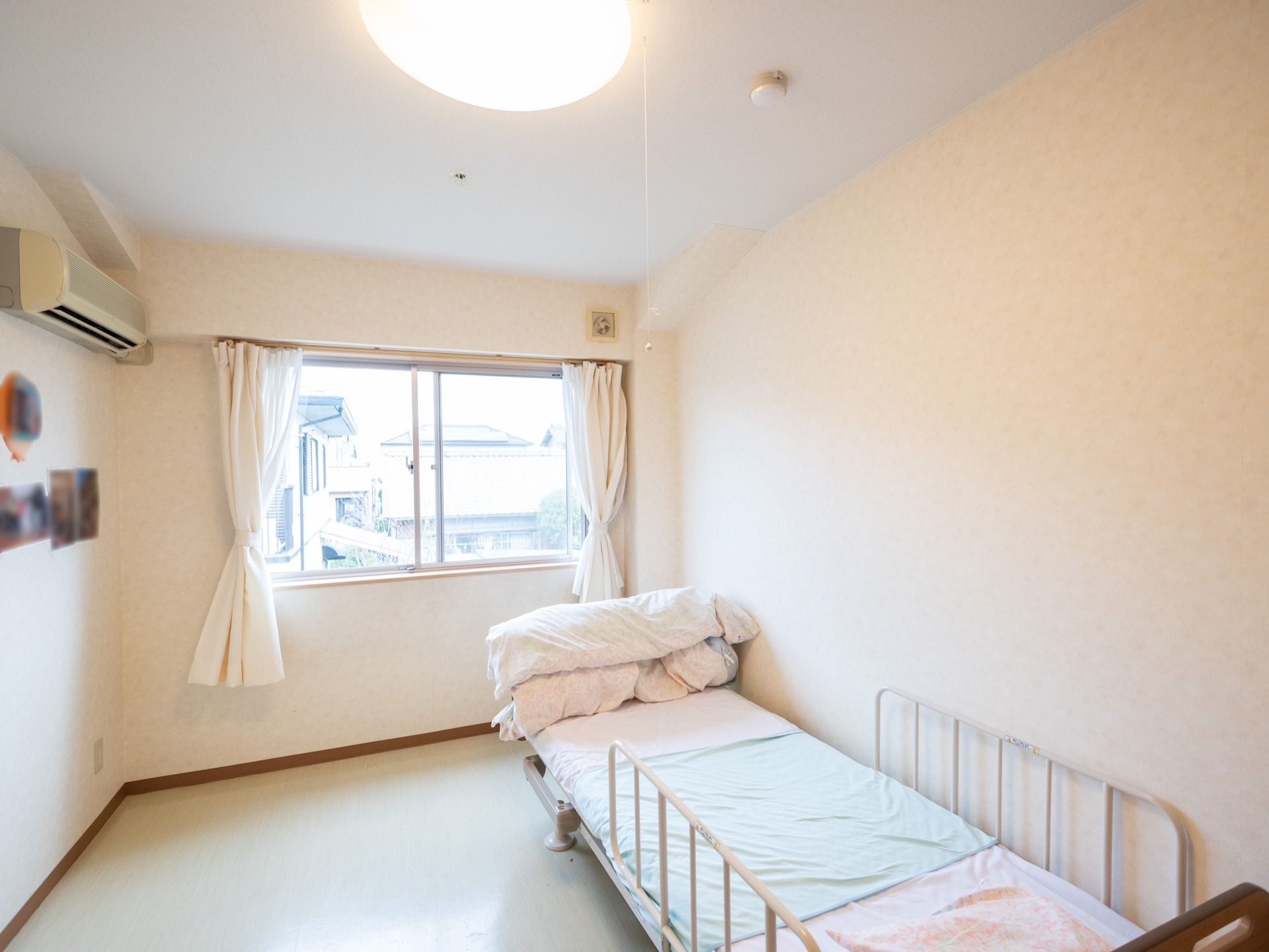 白を基調とした清潔感あふれる明るい部屋。エアコンが完備されており、壁際には転落防止用の柵が付いたベッドが置かれている。