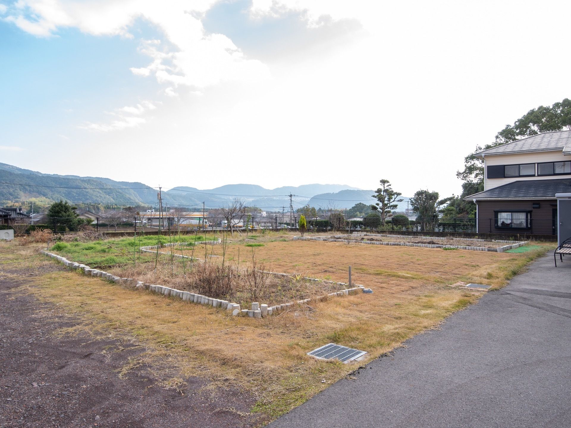 施設近くの開けた場所に芝生広場がある。円柱状のブロックを並べて縁どりをした花壇がある。遠くに山並みが見える。