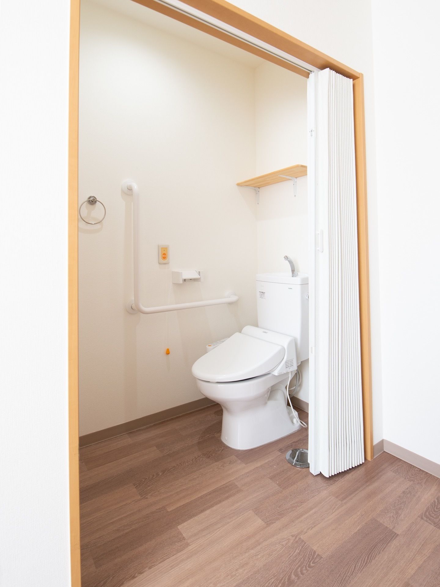 トイレは、じゃばらのカーテンで仕切られた広いスペースに設置されている。壁に、ナースコールボタンや手すりがある。