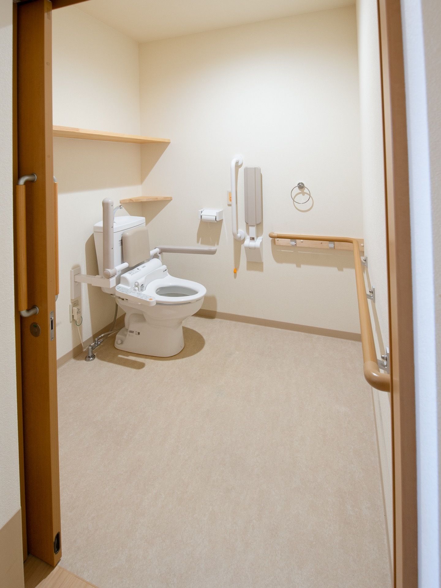トイレはスペース後方にある。便座の周りには可動式のひじ掛けや背もたれ、縦横の手すりがあり、つかまりながら立ち座りできる