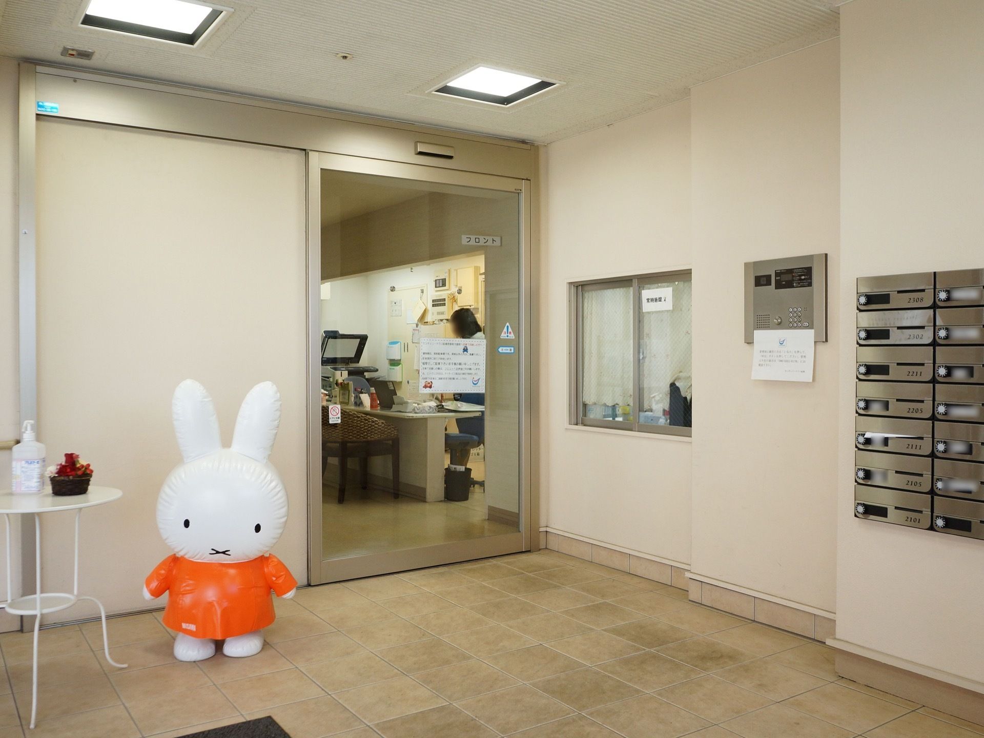 キャラクターの風船が置かれている玄関。自動ドアは大きく透明なガラスになっており、ポストはダイヤル式になっている。