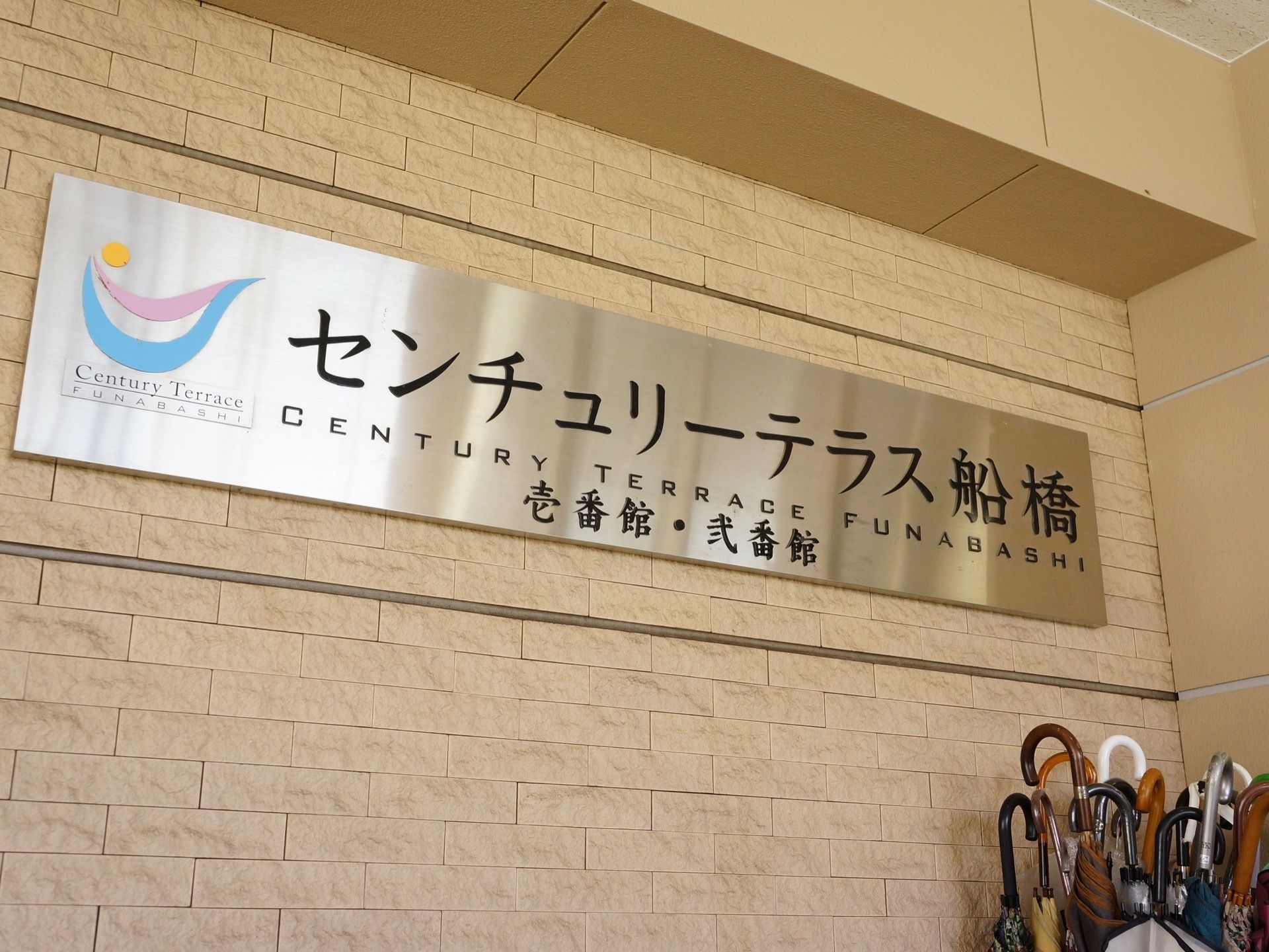 シルバーの板に大きく読みやすい黒い文字で施設の名前が書かれた看板。左側にはシンプルなロゴも入っている。