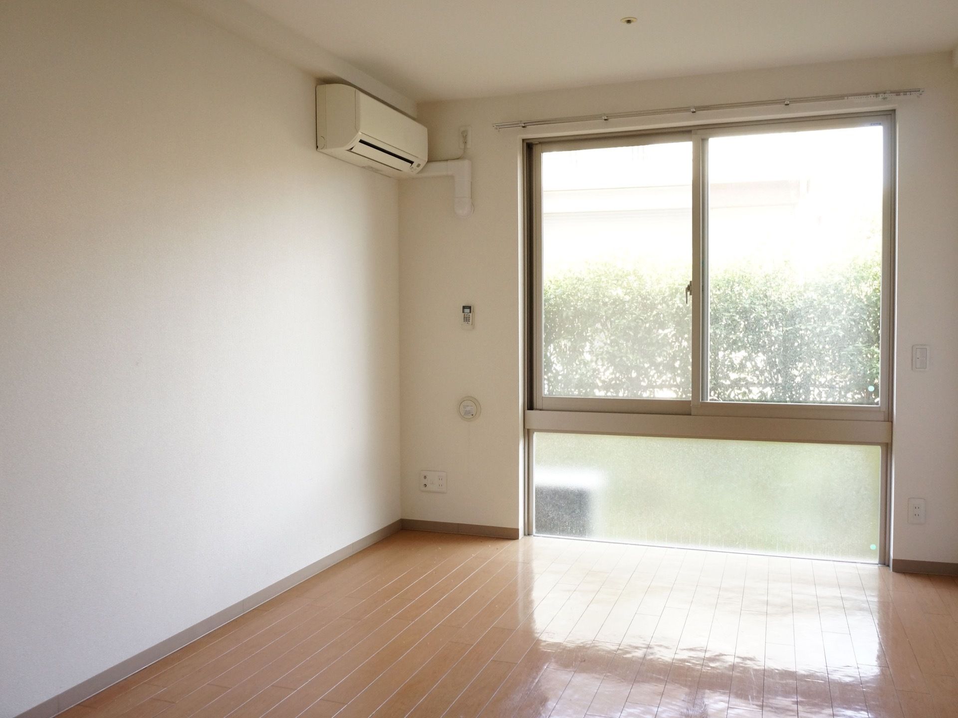 窓が広くて、陽光の差し込む明るい部屋である。天井、壁は白で床はフローリングと清潔感があふれる。壁にはエアコンが設置されている。