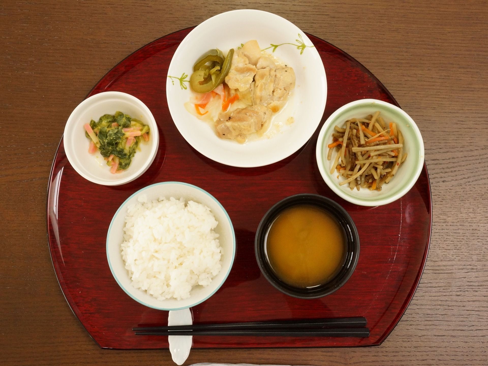 メインの料理のお皿の脇にきんぴらごぼうなどの副菜が２品とお味噌汁に白いご飯がおぼんの上に並んでいる。