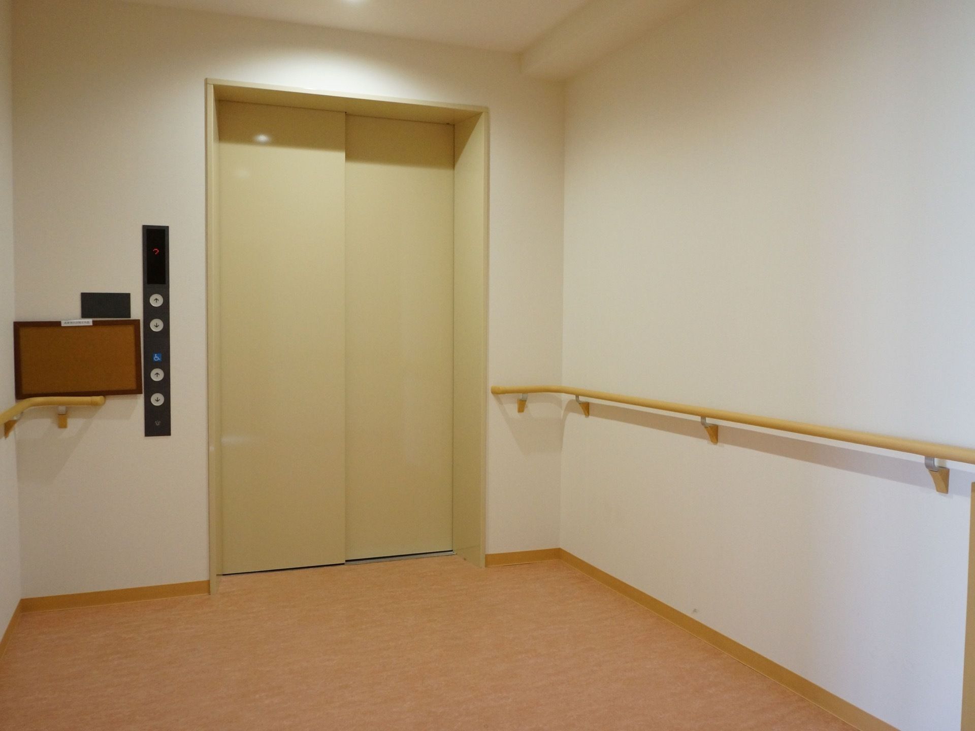 エレベーター周囲の壁には手すりが設置されている。扉の横にはコルクボードが貼られ、お知らせなどが貼りだされる。