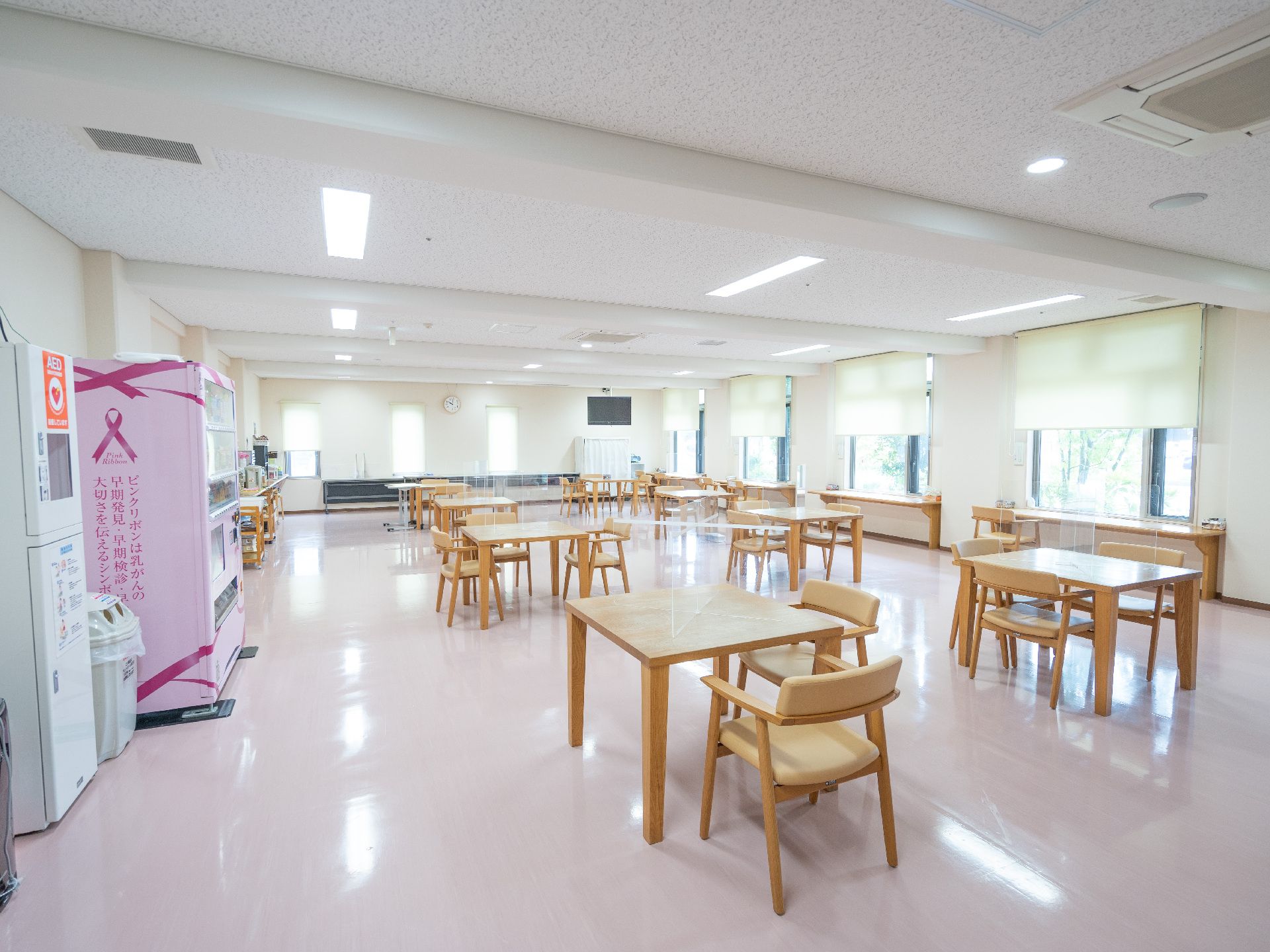 壁に大きな窓ガラスが配置された部屋に規則正しく並んでいる木製の机と椅子
