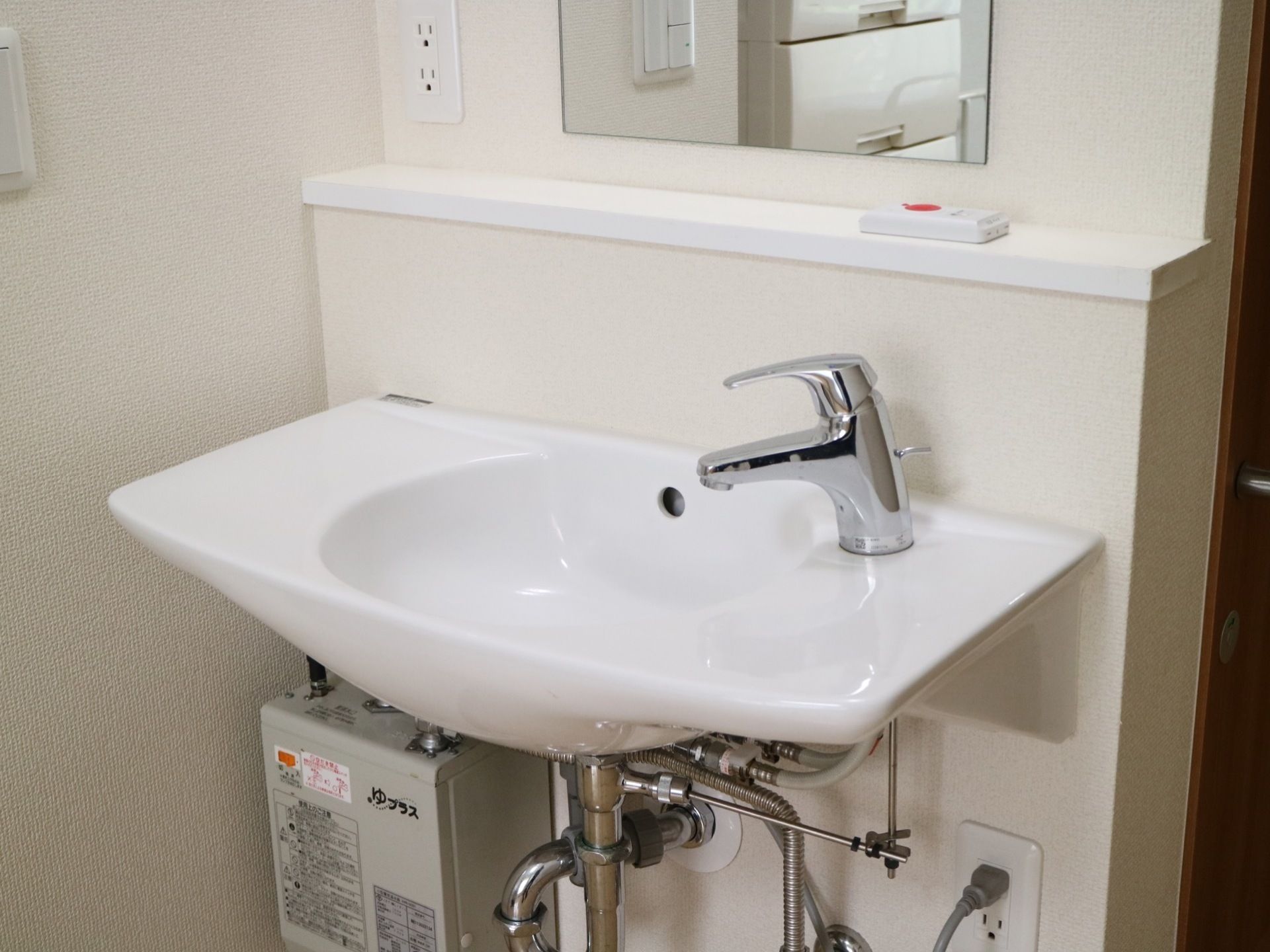フットレス設計の洗面台が居室に完備されており、蛇口からは水だけでなくお湯も出るようになっている。壁に鏡やコンセントがある。