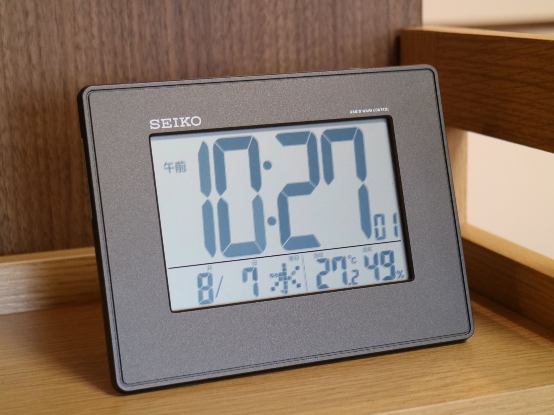 テーブルの上に置時計がある。デジタルタイプ。時刻が大きく表示され、日付や温湿度も確認できる。