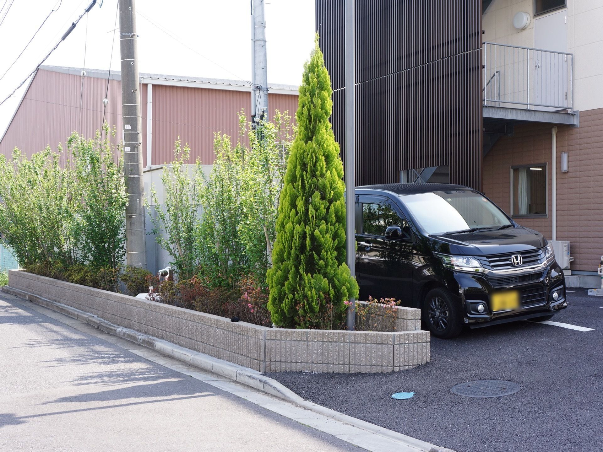 施設には非常階段が設置されている。黒い車が停まっており、駐車スペースが設けられている。植木もあり、キレイに手入れをされている。